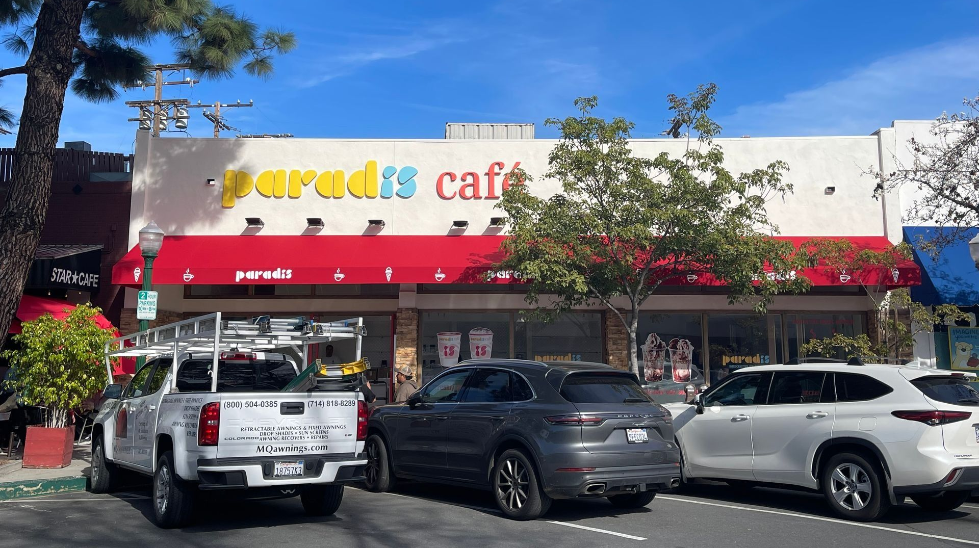 Paradise Cafe with a red awning, cars parked in front, and a clear blue sky.