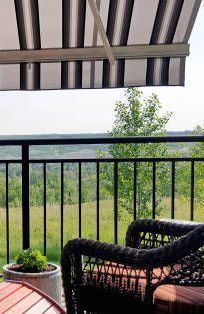 Patio with awning, wrought iron railing, wicker chair, and view of trees.