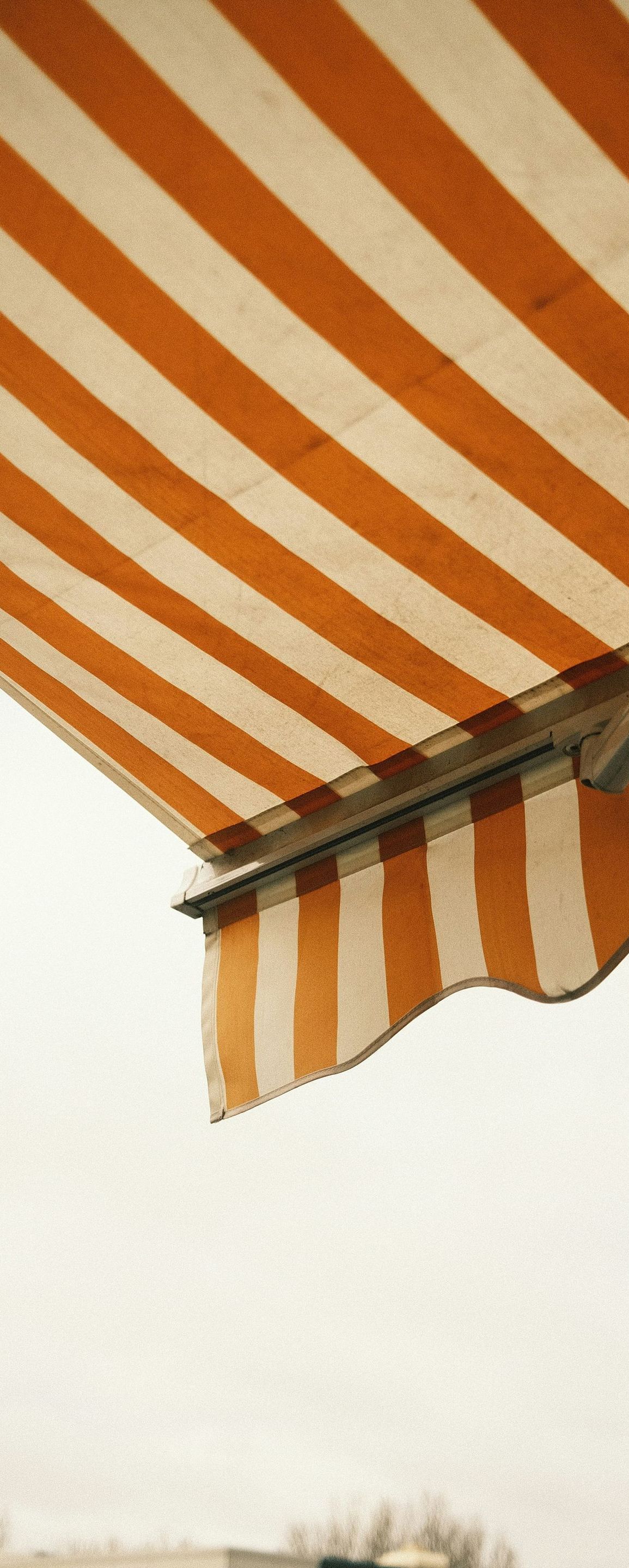 A close up of an orange and white striped awning against a cloudy sky.
