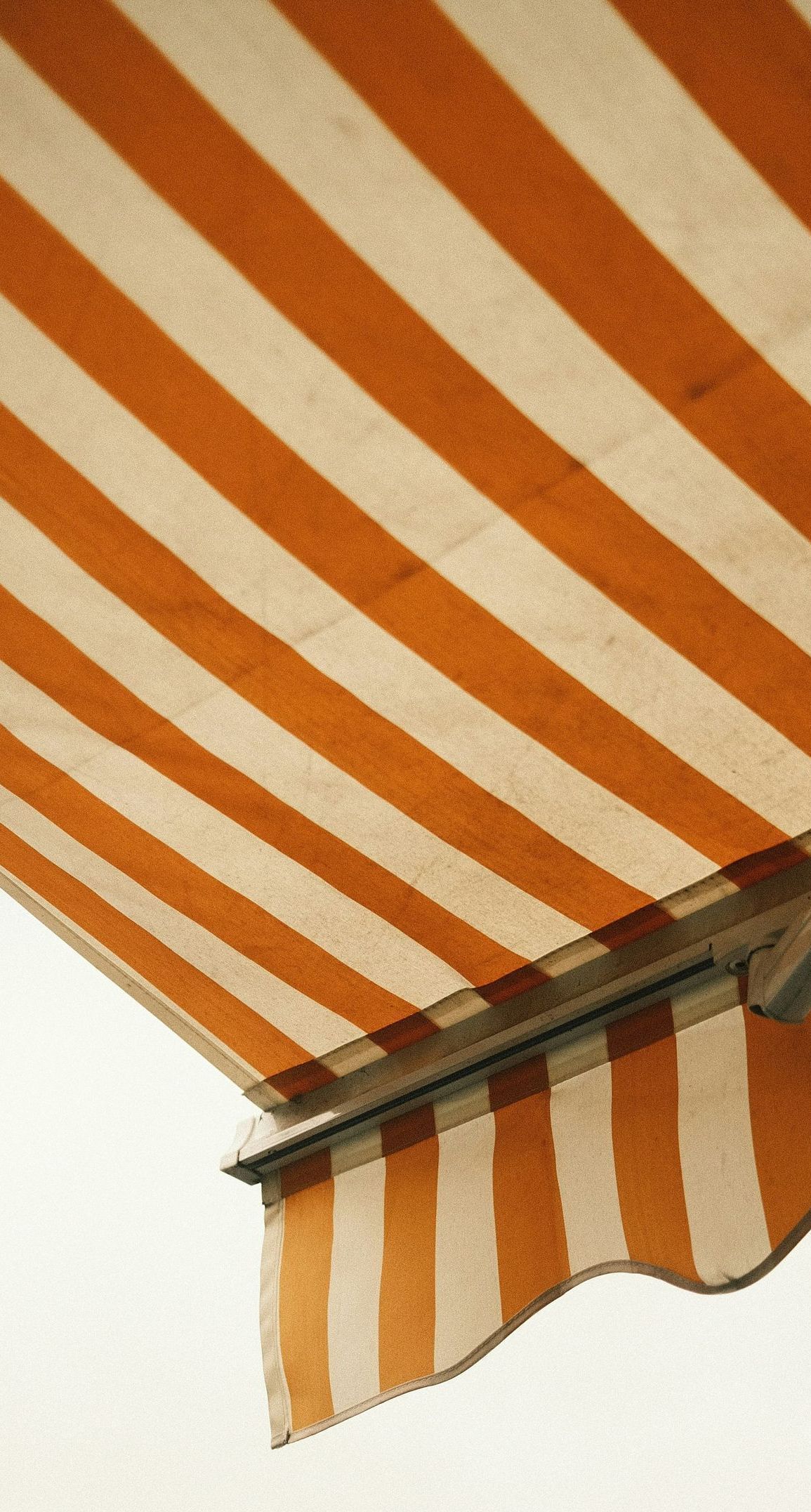 A close up of an orange and white striped awning against a cloudy sky.