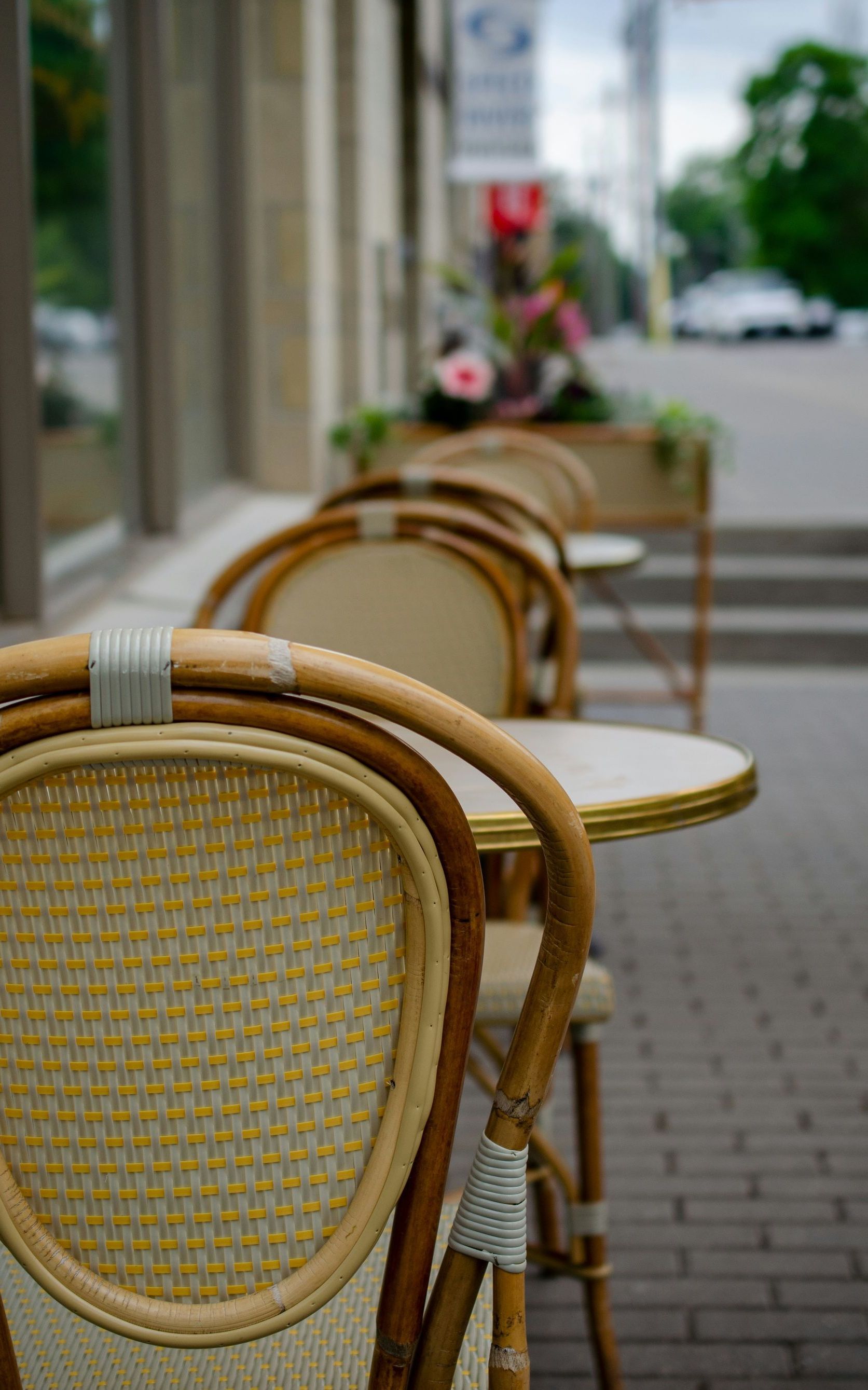 A row of wicker chairs and tables outside of a restaurant.