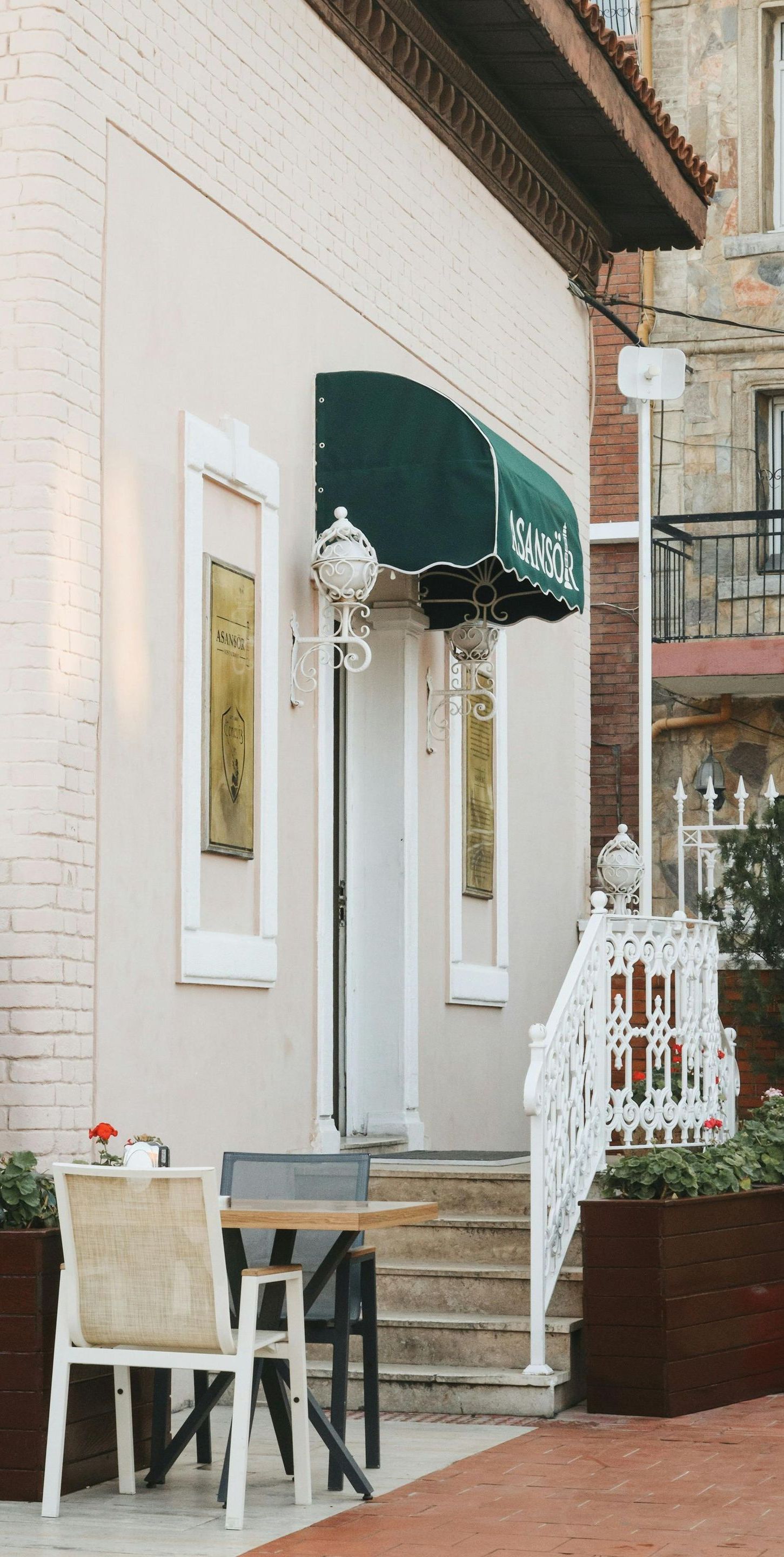 A white building with a green awning and a table and chairs in front of it.