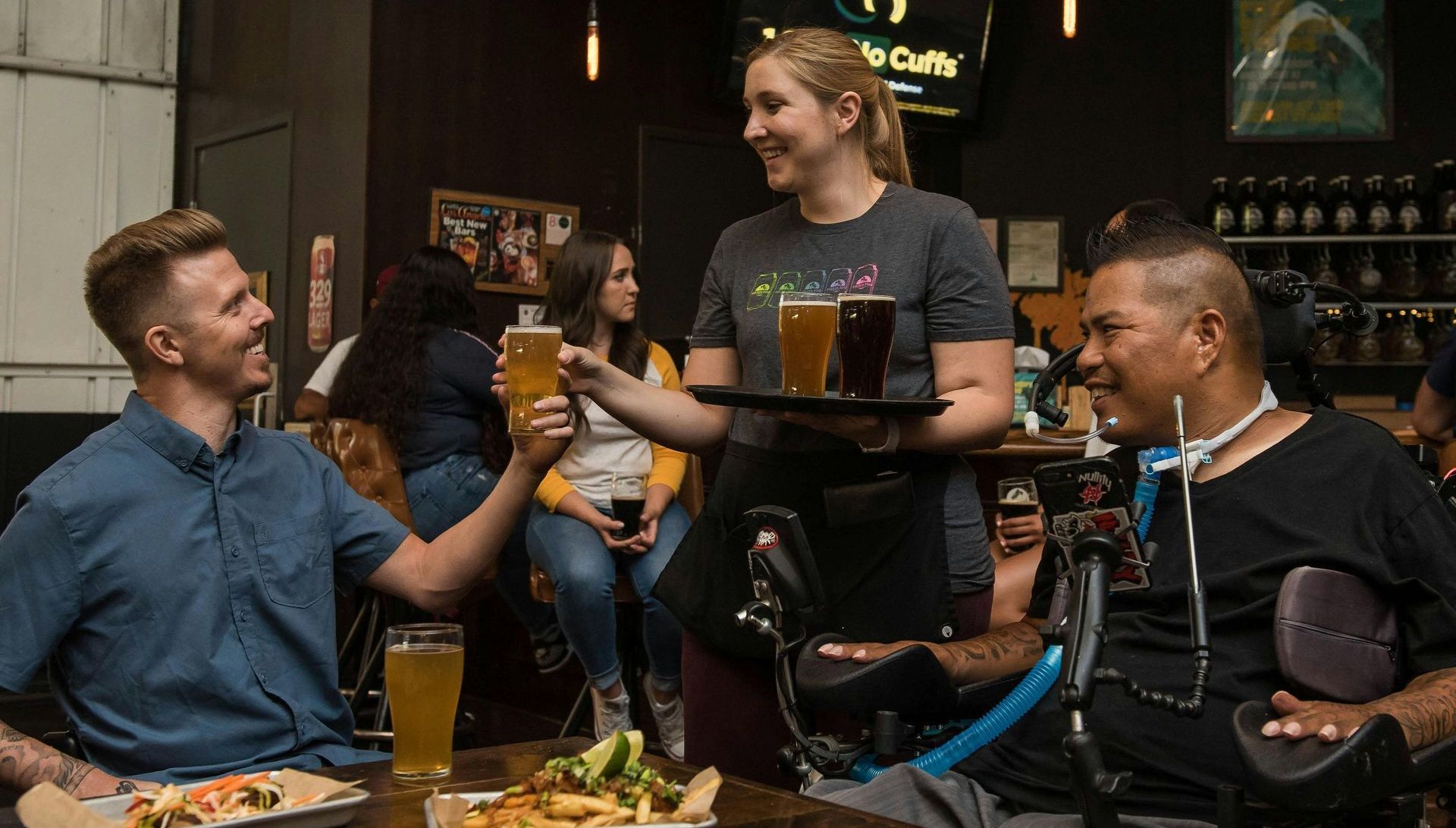 A woman is serving beer to a man in a wheelchair at a restaurant.