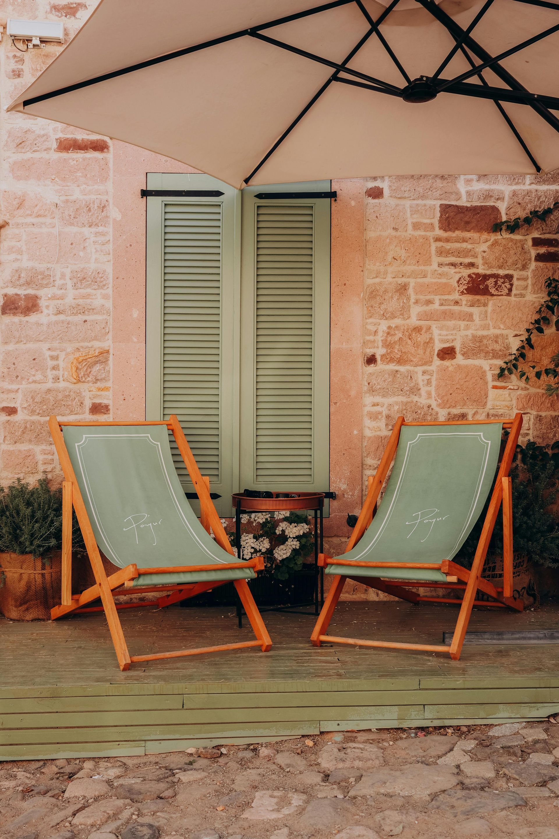 Two lawn chairs under an umbrella in front of a brick building.
