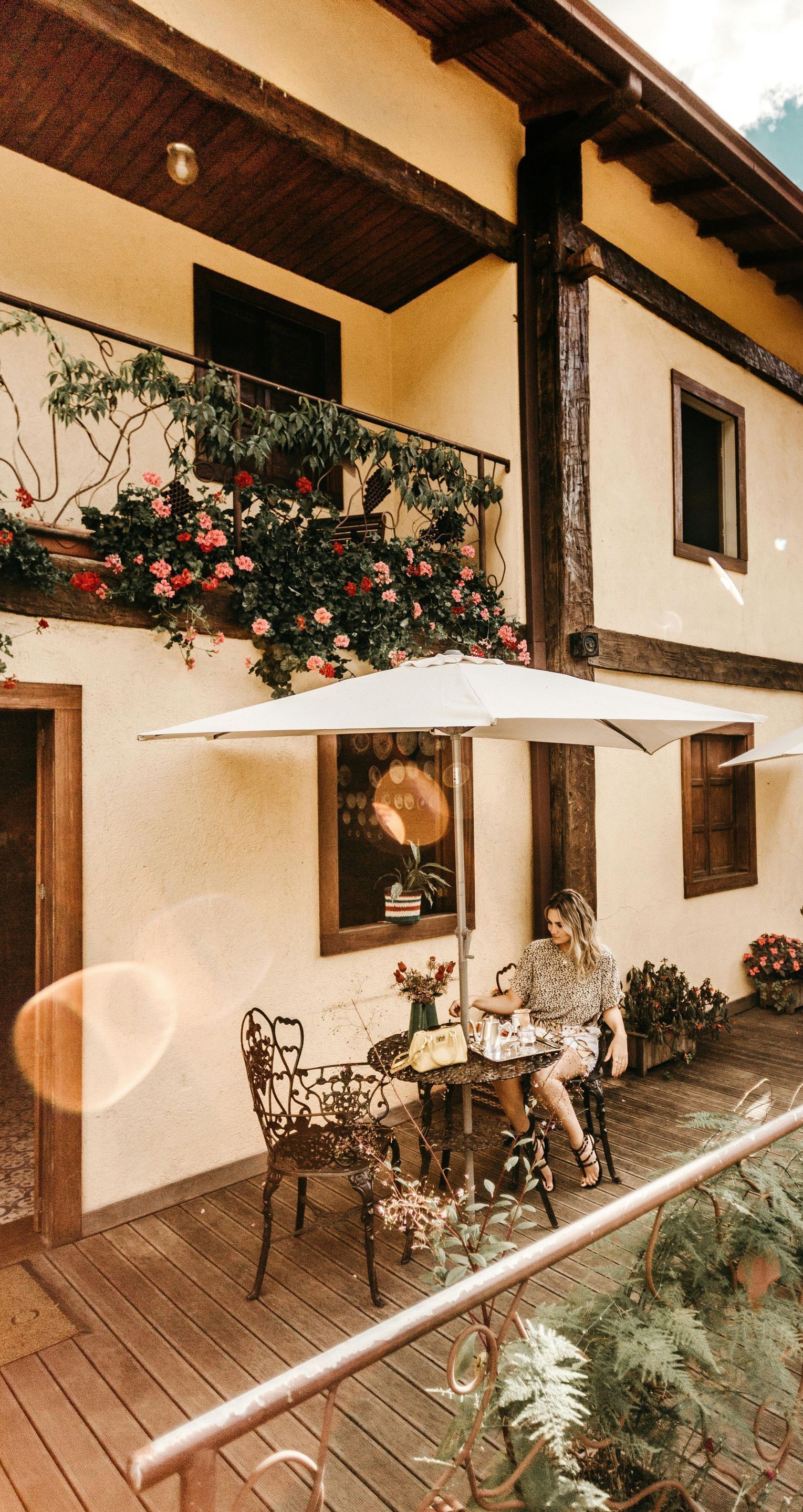A woman is sitting at a table under an umbrella in front of a building.