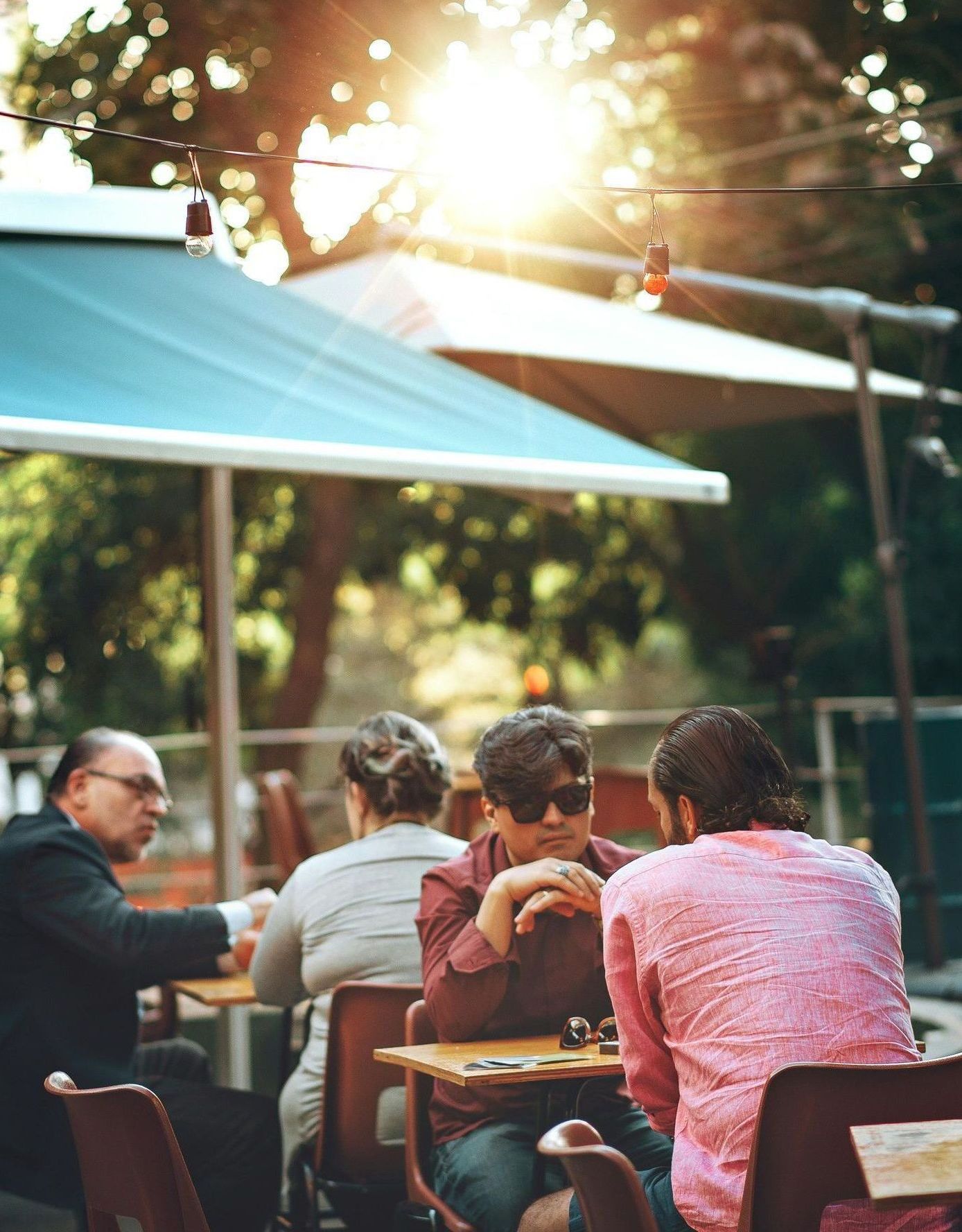 A group of people are sitting at tables outside under umbrellas.