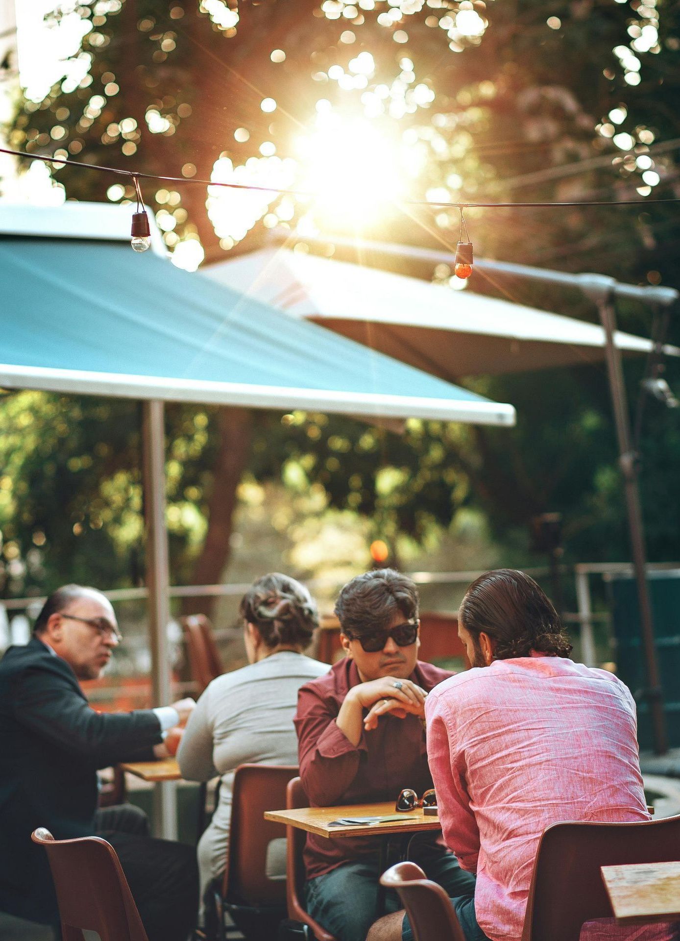 A group of people are sitting at tables outside under umbrellas.