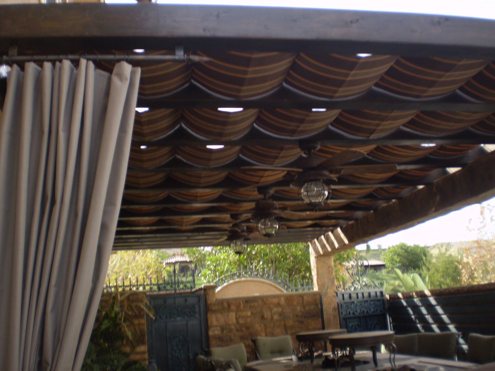 Pergola with striped canopy, tan curtains, and outdoor seating area.