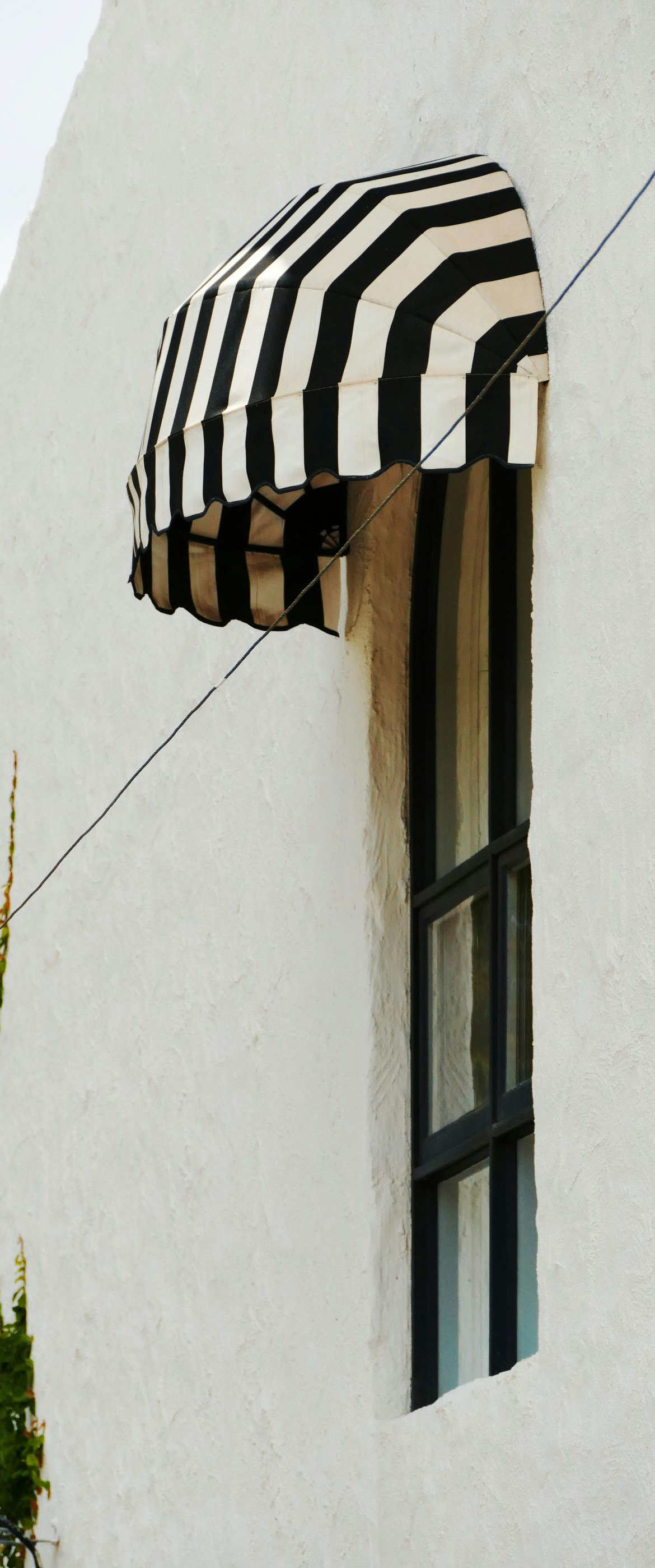 A window with a black and white striped awning on a white building.