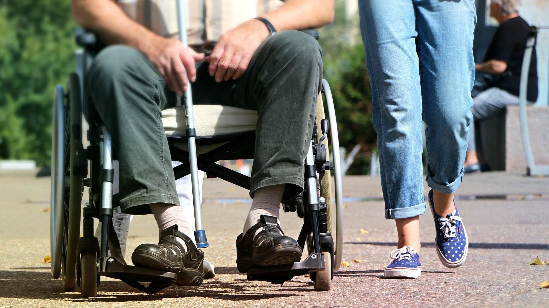 A woman is walking next to a man in a wheelchair.