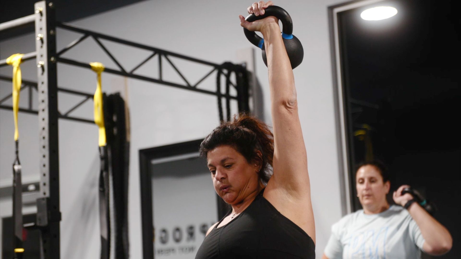A woman is lifting a kettlebell over her head in a gym.