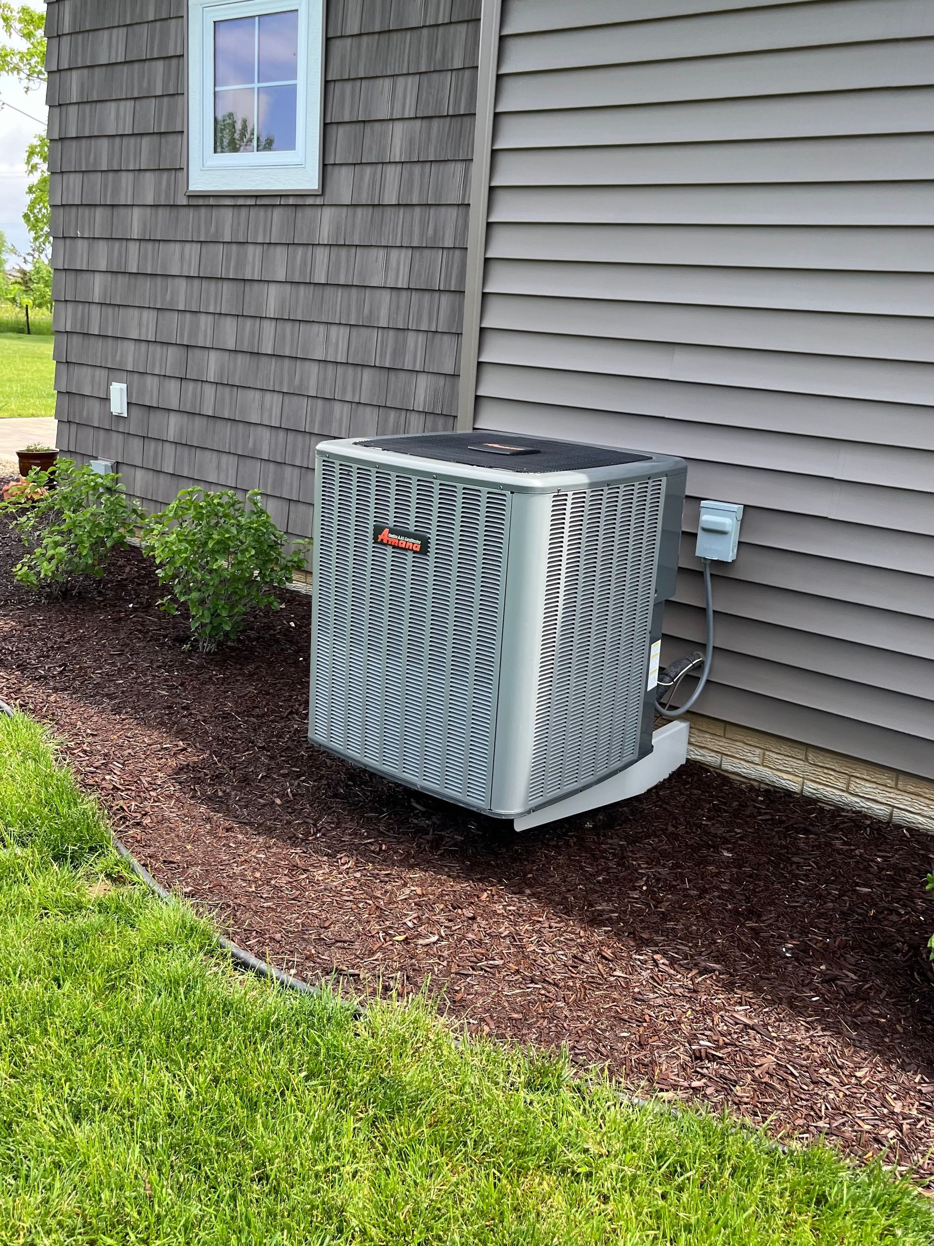 Comfort Pro - An air conditioner is sitting on the side of a house next to a window.