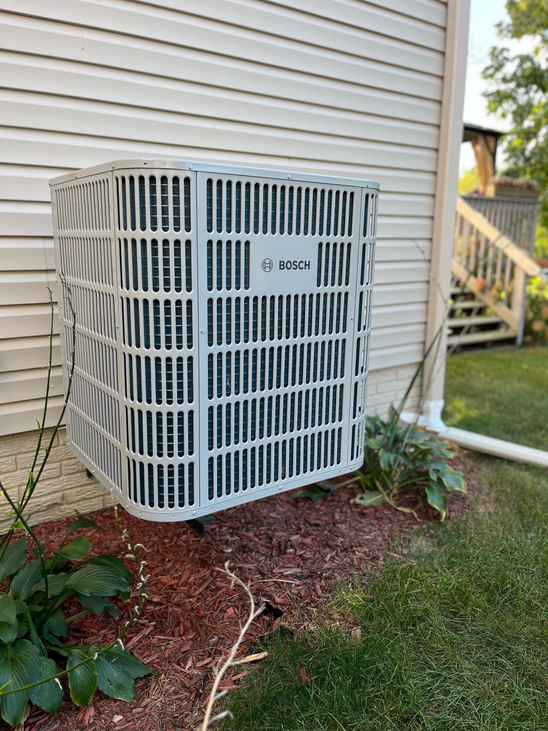 Comfort Pro - A white air conditioner is sitting on the side of a house.
