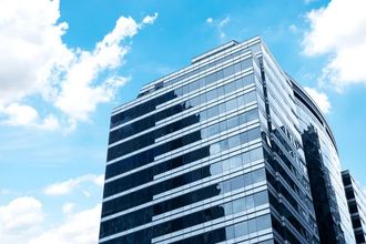 Modern glass skyscraper against a bright blue sky with fluffy white clouds.