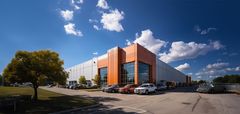 A large commercial building with an orange accent facade under a bright blue sky with white clouds; cars are parked in front.
