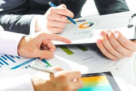 Business people reviewing financial reports with charts and a tablet. One person points to a chart.