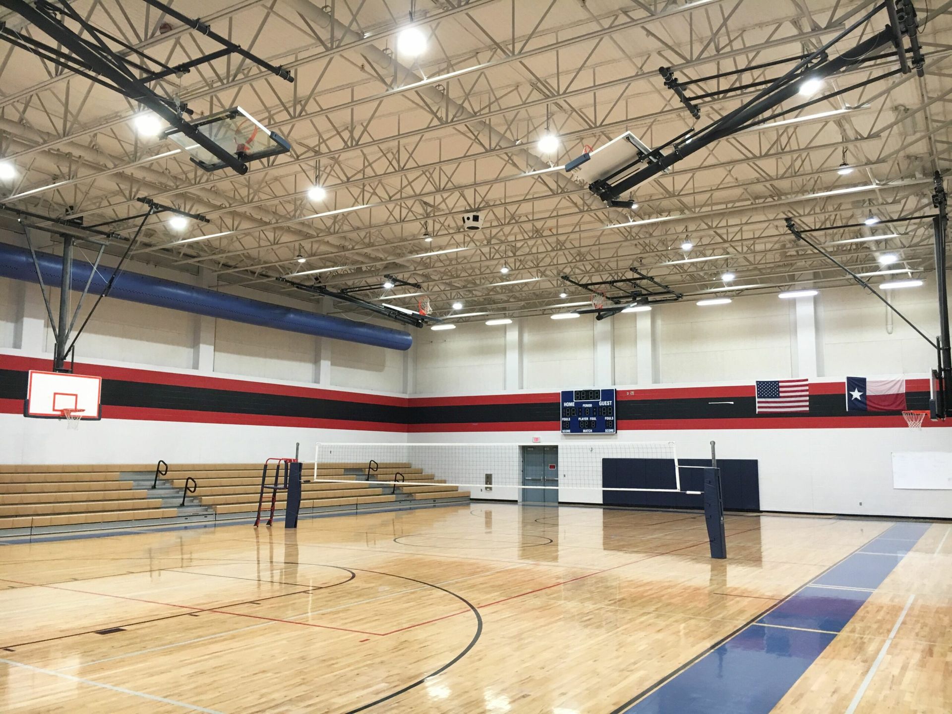 An empty gym with a basketball hoop and a volleyball net.