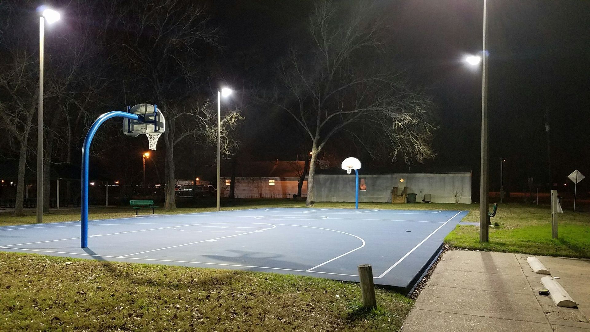 A basketball court is lit up at night in a park.