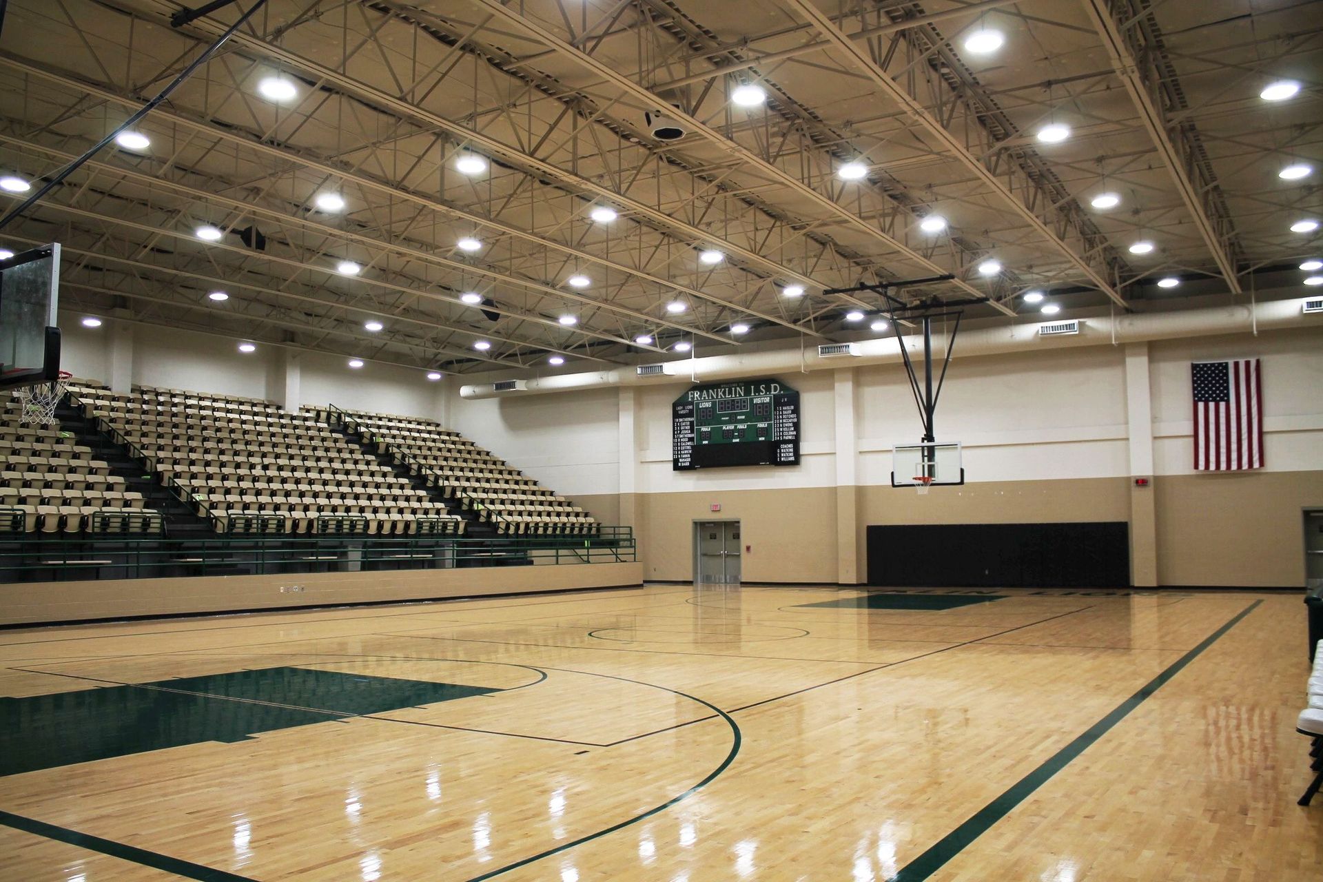 An empty basketball court with bleachers and an american flag