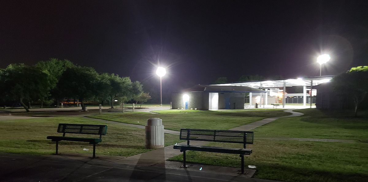 A park at night with two benches and a building in the background.