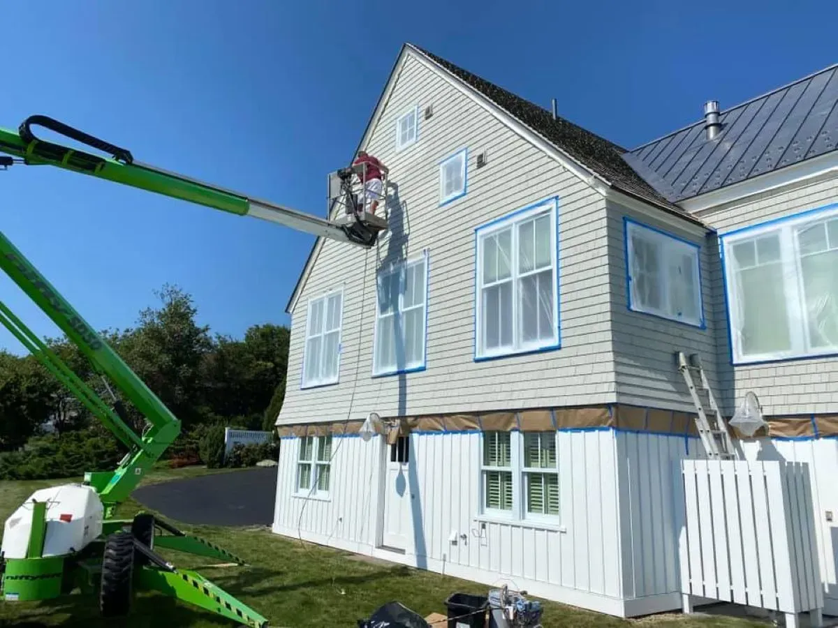 A green crane is painting the side of a house.