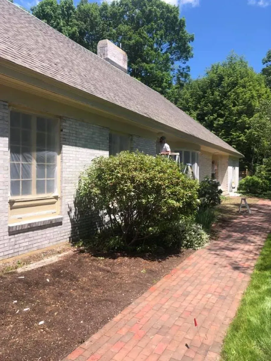 A white brick house with a gray roof and a brick walkway leading to it.