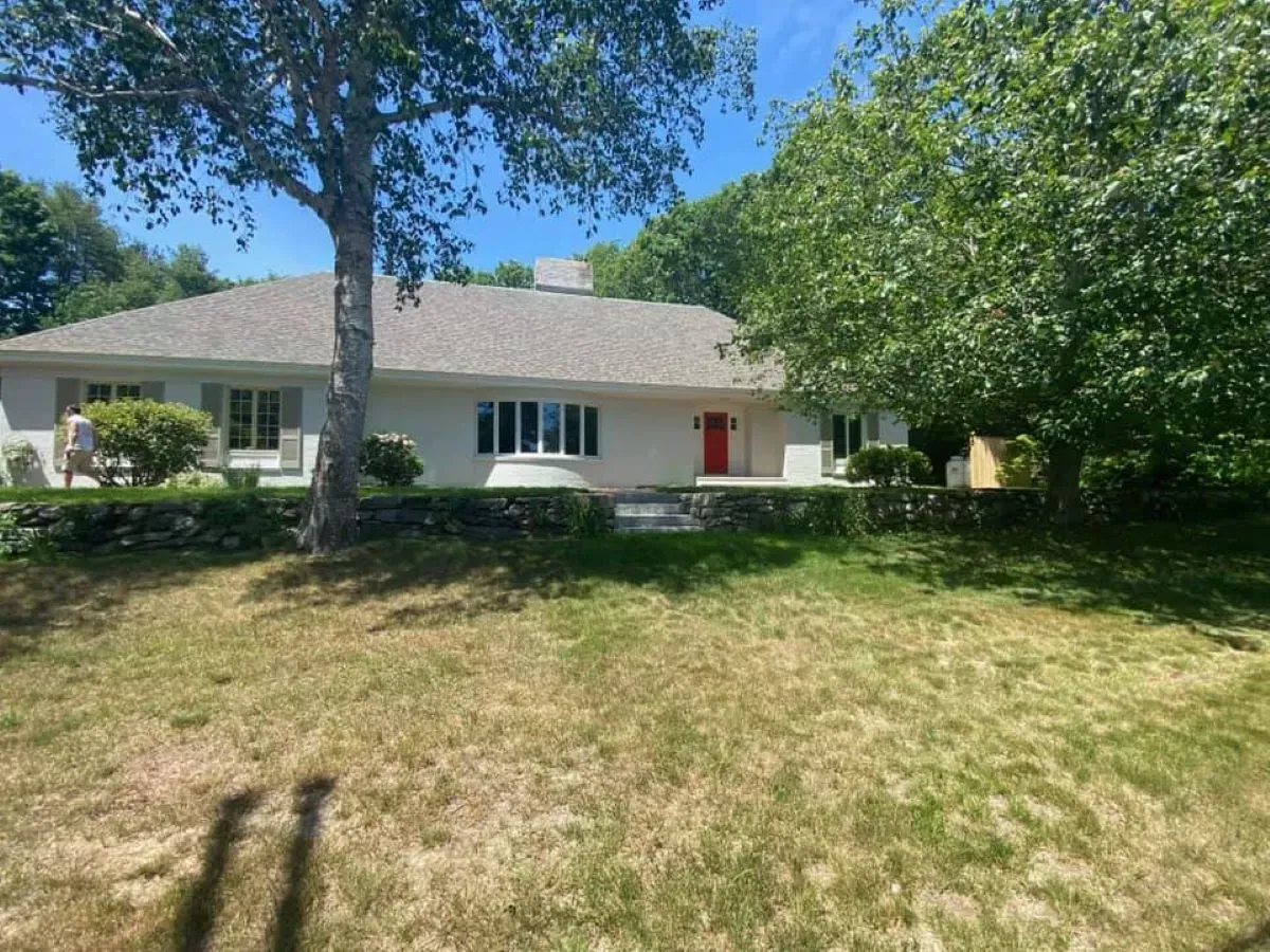 A white house with a red door and a tree in front of it