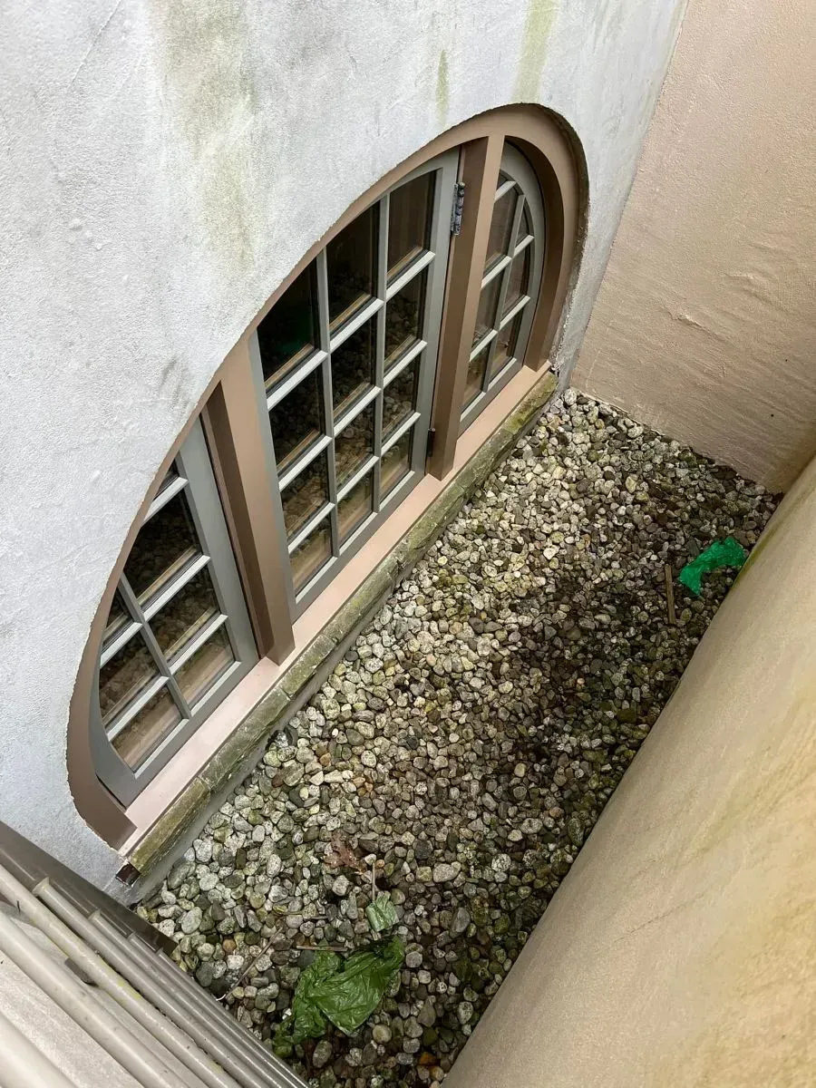 A window with a grid on it is sitting on top of a pile of gravel.