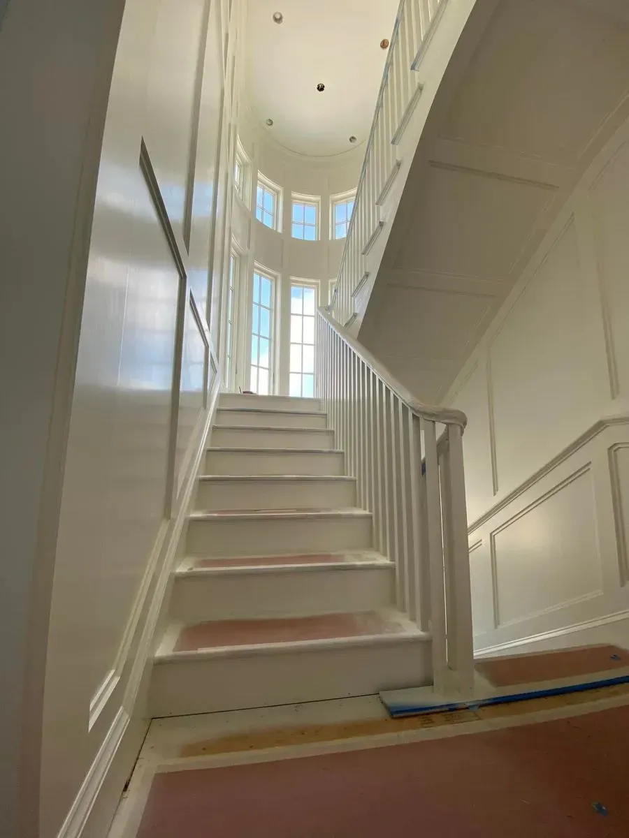 A staircase in a house with white walls and a pink carpet.