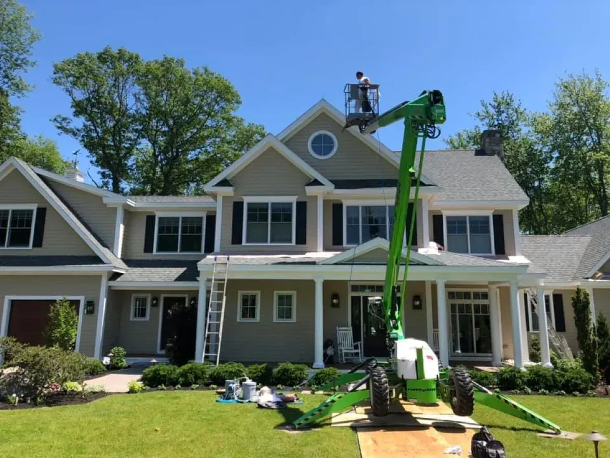 A large house is being painted by a green crane.