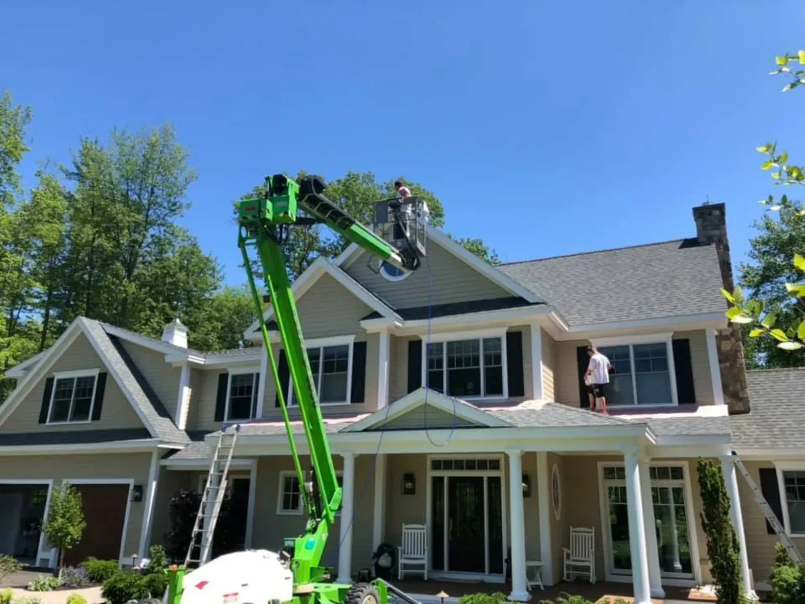 A man is painting the roof of a house with a green crane.
