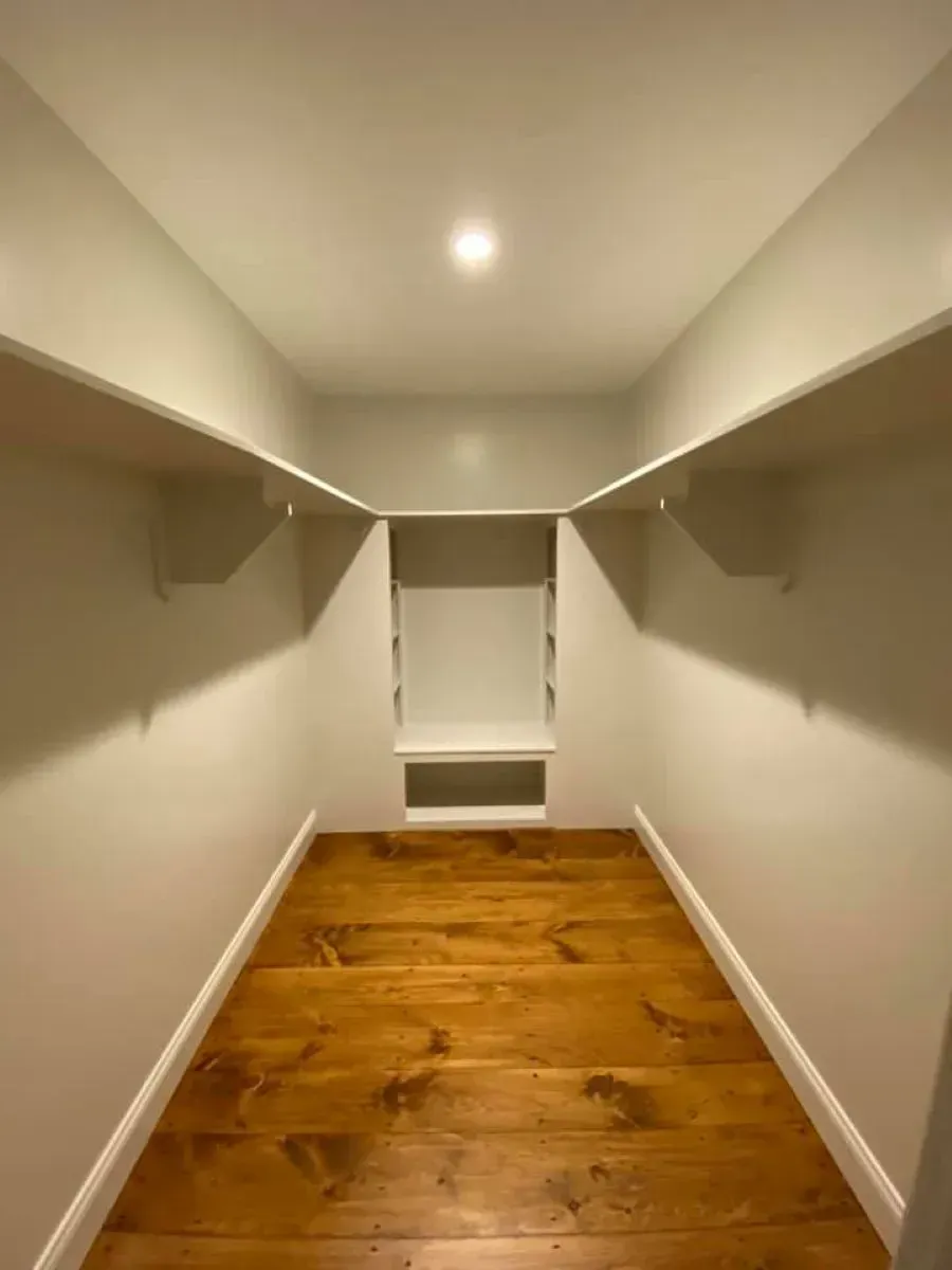 A walk in closet with wooden floors and white walls.