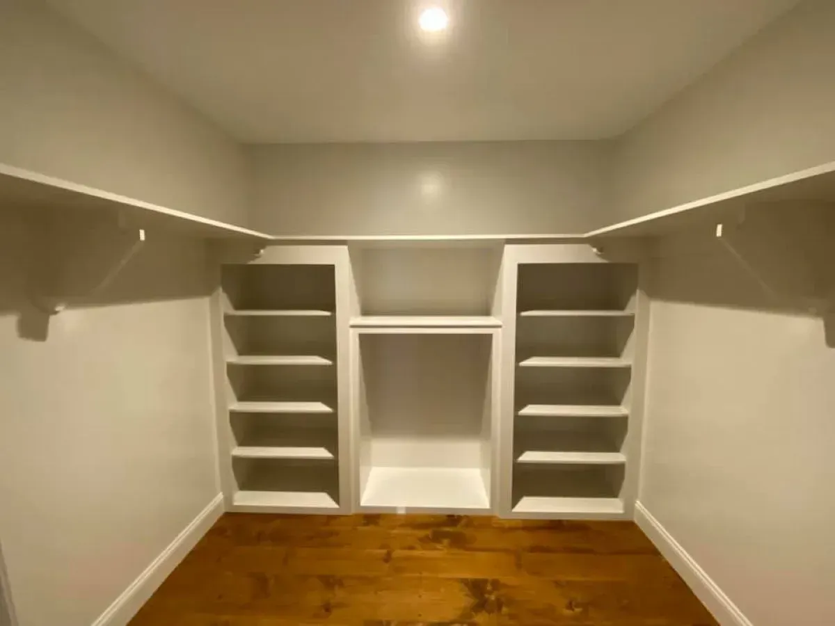 A walk in closet with white shelves and wooden floors.