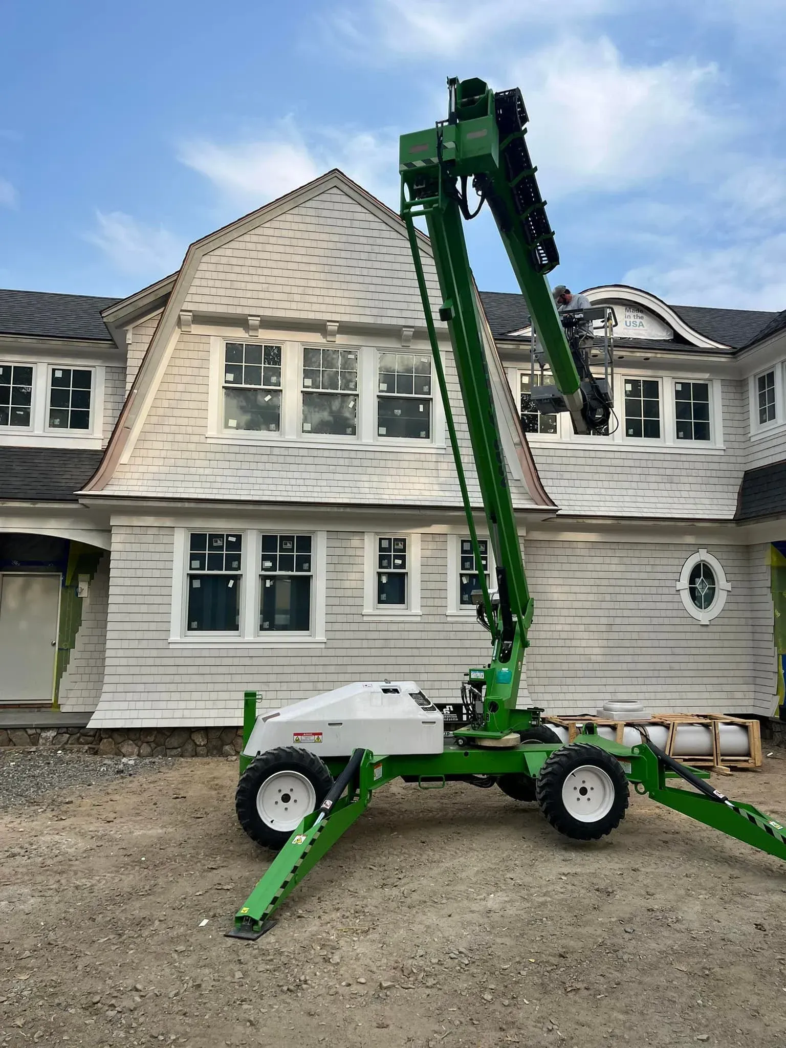 A green crane is parked in front of a large white house.