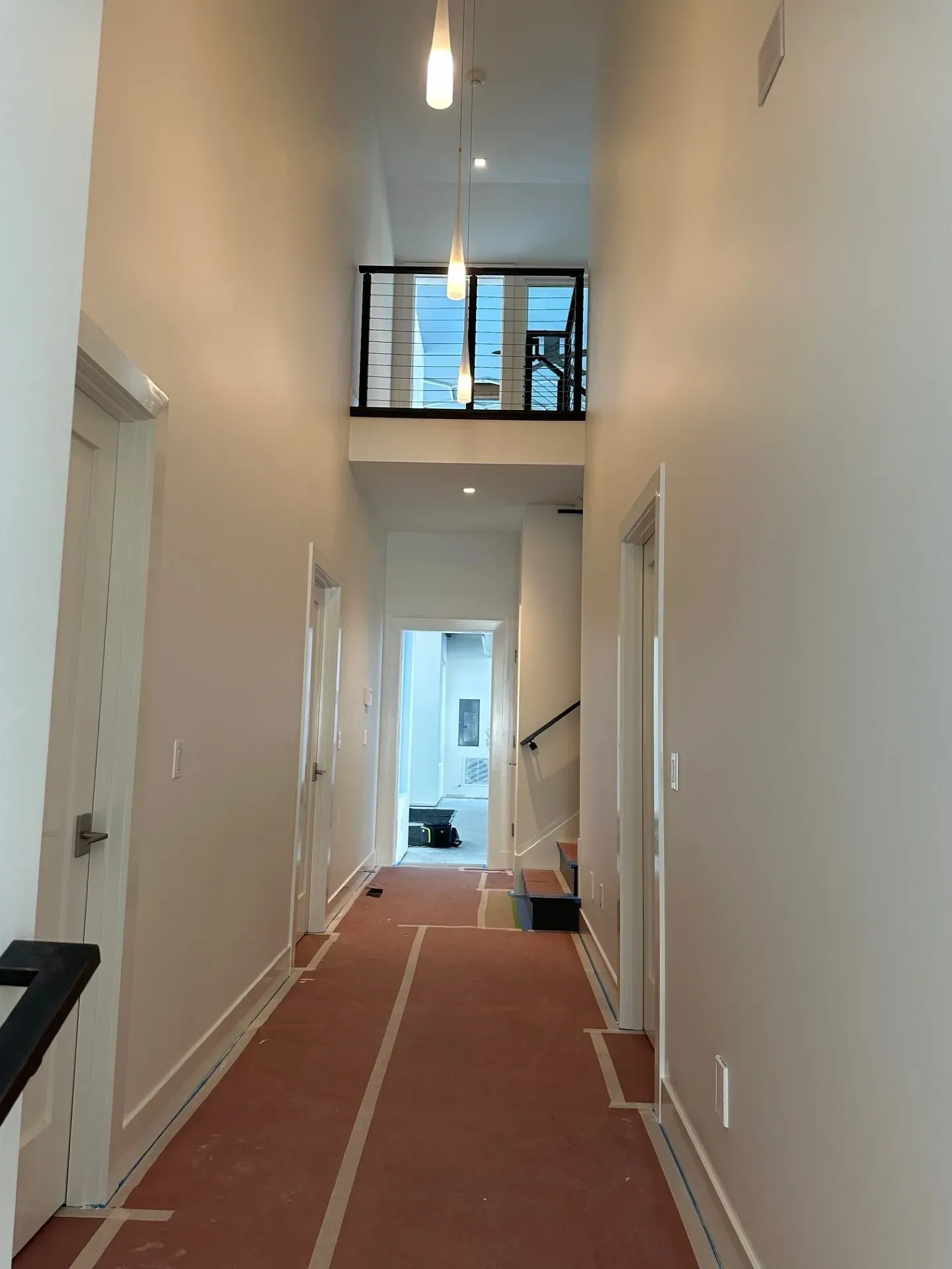 A long hallway in a house with white walls and a red carpet.