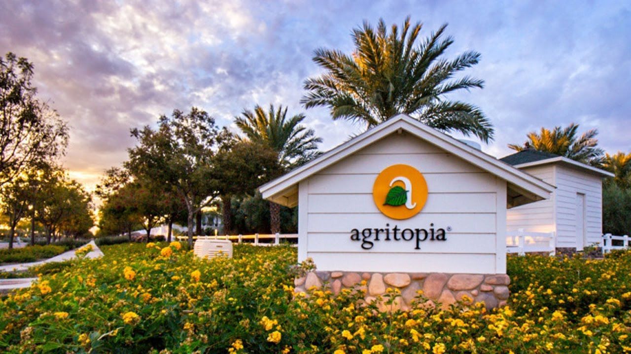 A white house with a sign that says agritopia in front of a field of yellow flowers.