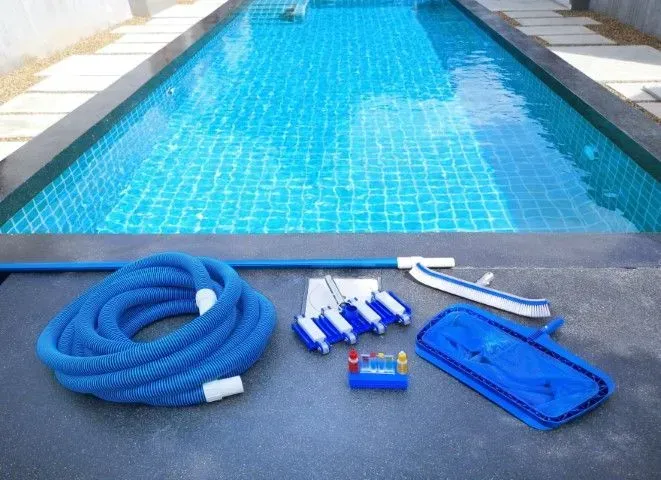Essential swimming pool cleaning tools including hoses and skimmers on the deck.