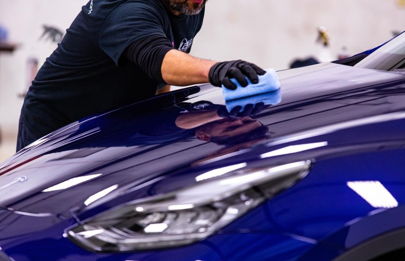 A man is cleaning the hood of a blue car with a cloth.