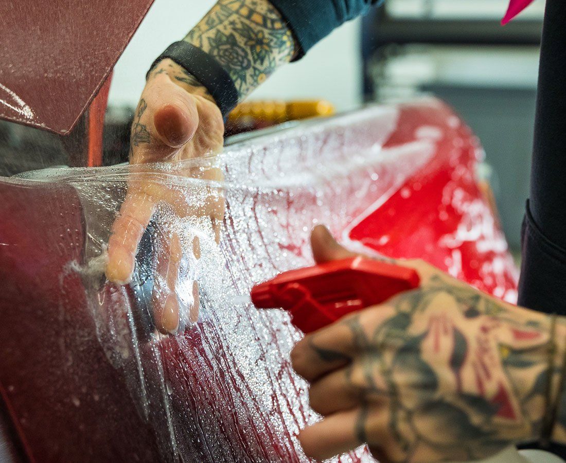 A person with tattoos is spraying a red car with a spray bottle.