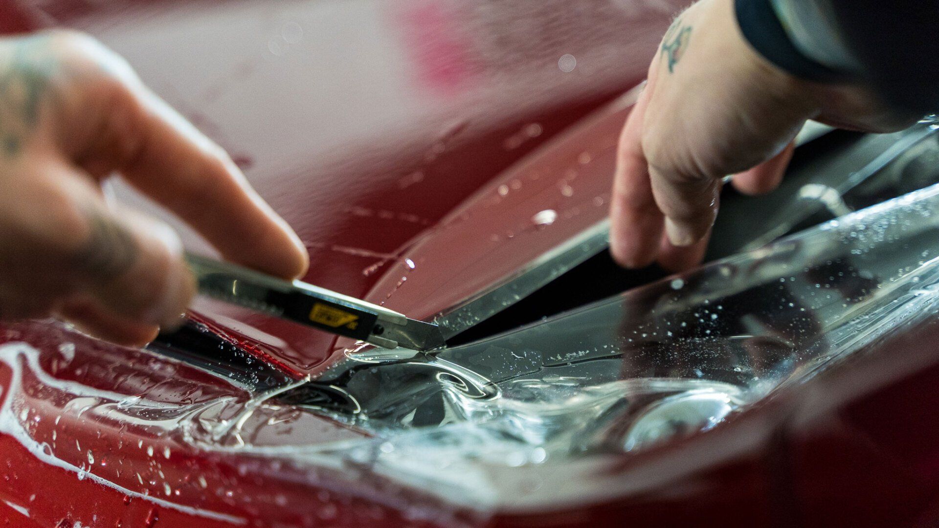 A person is cutting a piece of plastic on a red car.