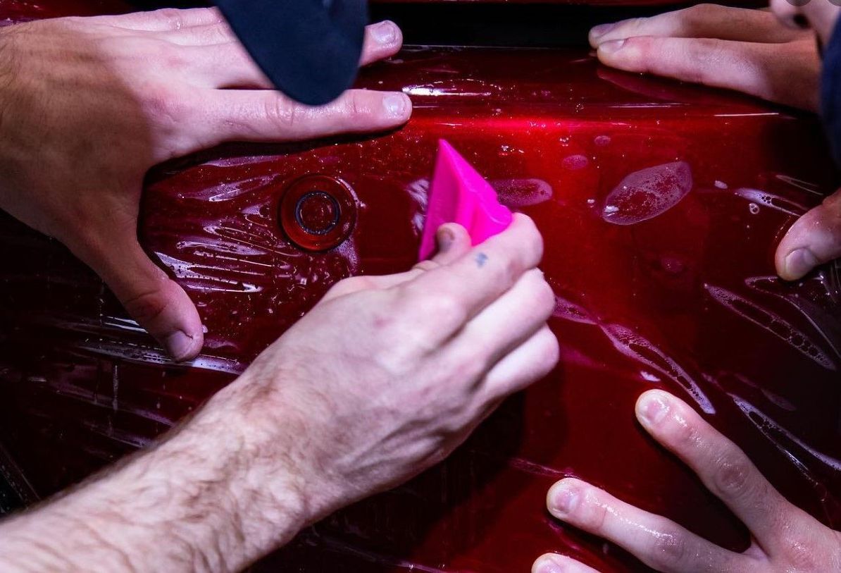 A man is holding a pink spatula over a red car.