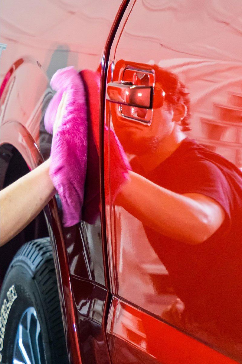 A person is cleaning a red car with a pink cloth