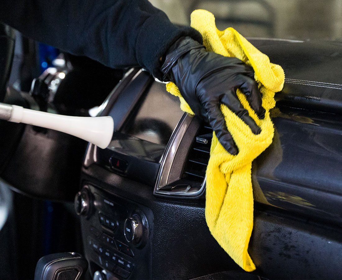 A person wearing black gloves is cleaning the dashboard of a car with a yellow towel.
