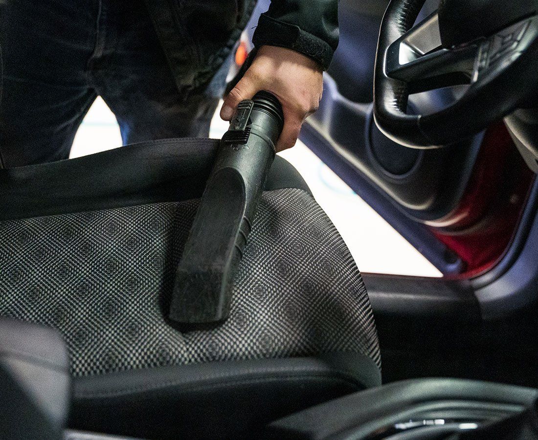 A person is cleaning a car seat with a vacuum cleaner