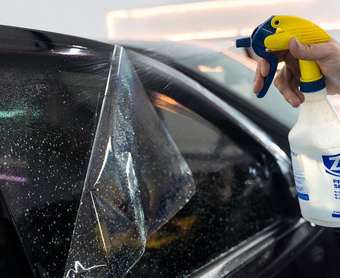 A person is spraying a car window with a spray bottle that says z on it