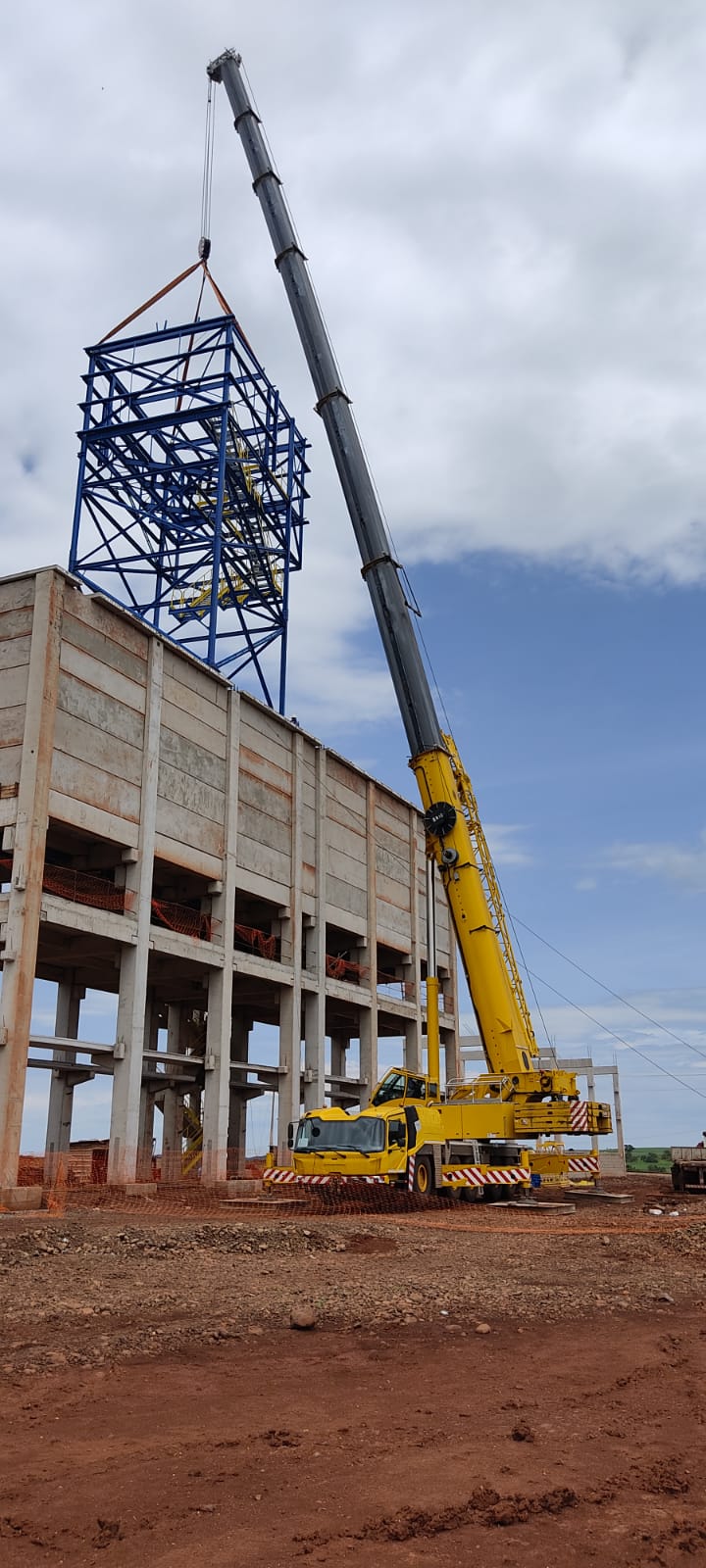 Um grande guindaste amarelo está levantando uma estrutura no topo de um edifício.