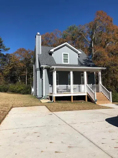A small house with a porch and a driveway in front of it.