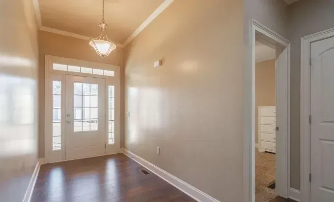 A hallway in a house with a door and a chandelier.