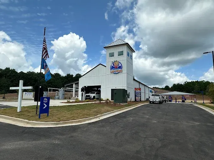 A white building with cars parked in front of it and a cross in front of it.