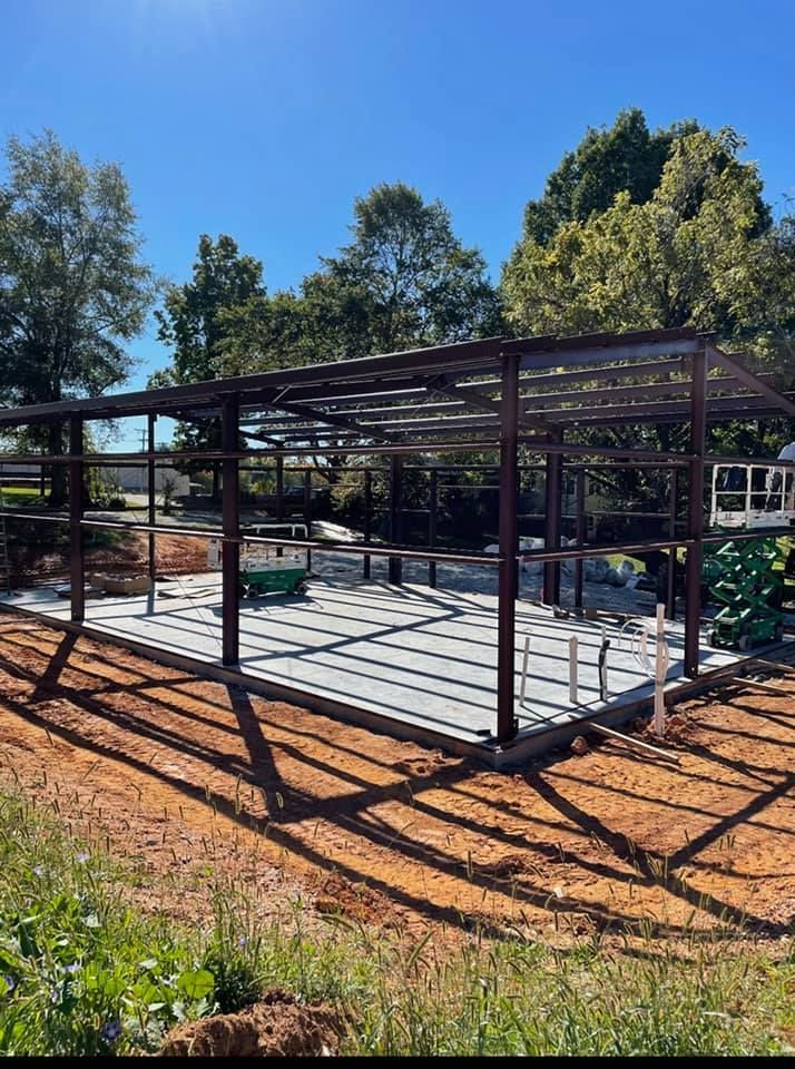 A metal structure is being built in a field with trees in the background.